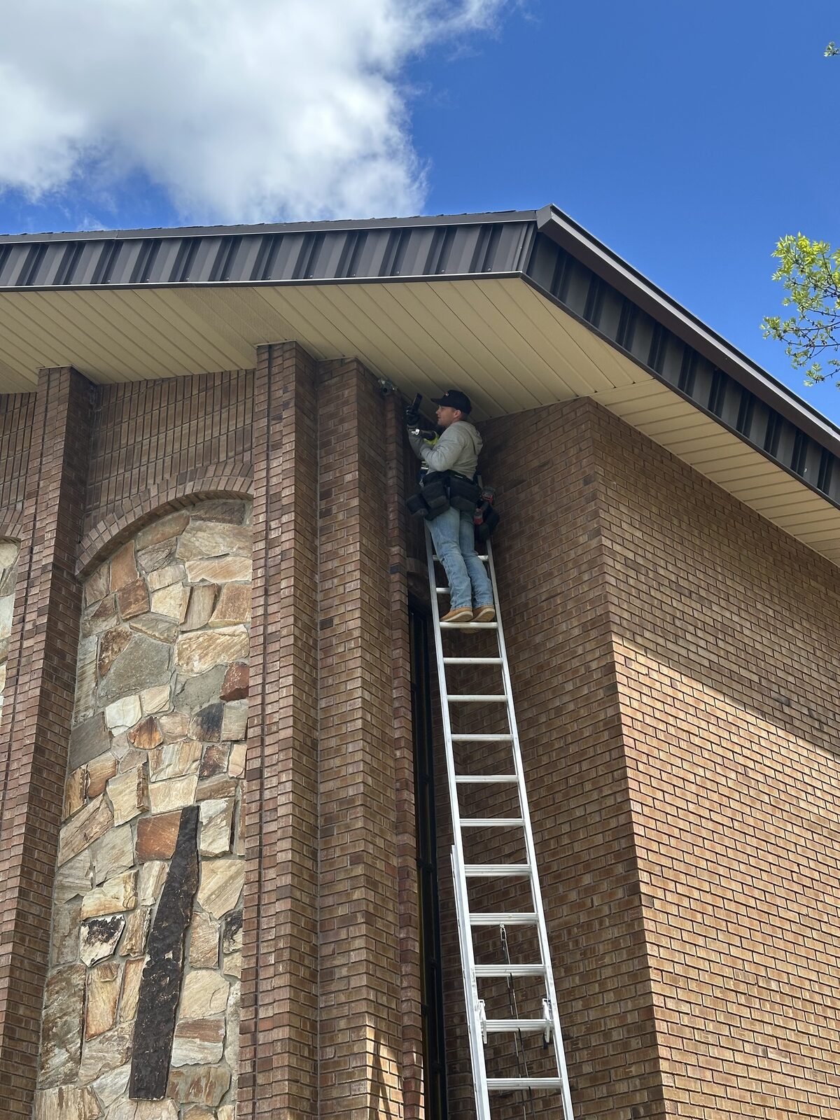 Technician on a ladder sealing bat entry points at a church roofline